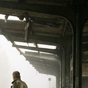 A man at the abandoned Berlin-Wannsee 1958 station near a rusted steam engine.