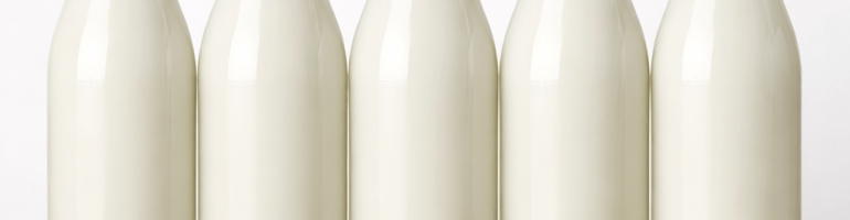 Five glass bottles filled with white milk standing upright on a wooden table