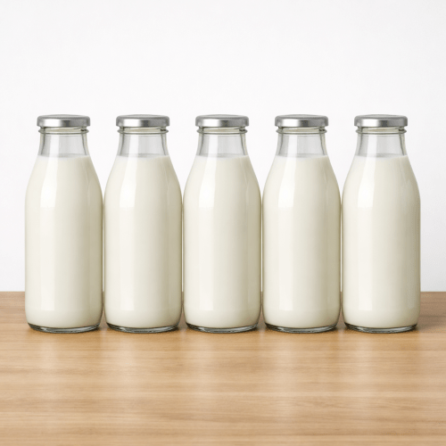 Five glass bottles filled with white milk standing upright on a wooden table