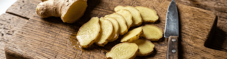 Fresh ginger root and thin ginger slices on a wooden cutting board with a knife