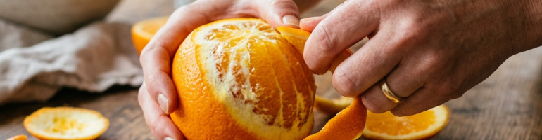Hands peeling the skin off a fresh orange on a wooden table