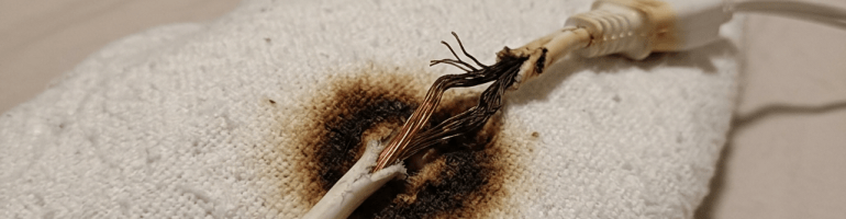 Burned electrical cord with exposed wires and scorch mark on white fabric
