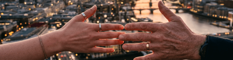 Two hands nearly touching on a rooftop with London cityscape and sunset in background