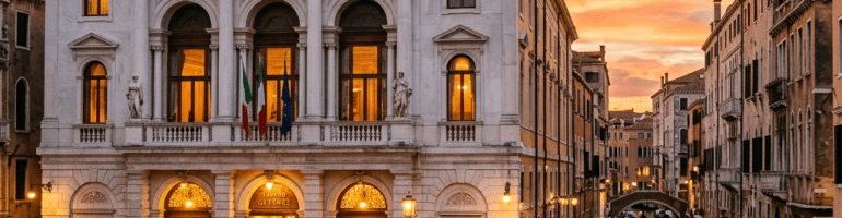 Teatro La Fenice opera house with people outside and gondolas on a canal at sunset