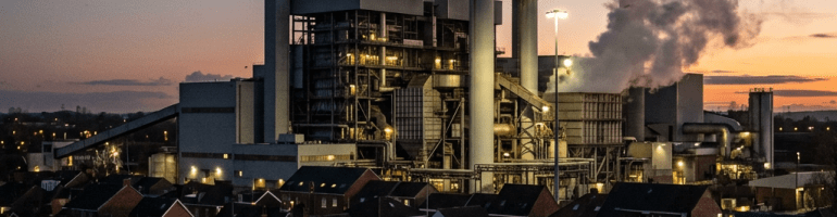 Industrial power plant with tall smokestacks emitting smoke near residential neighborhood at dusk