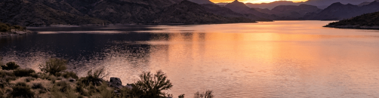 Sunset over a mountain lake with colorful sky and a person sitting near water