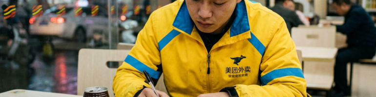 Delivery worker in yellow uniform writing in a notebook at a café table