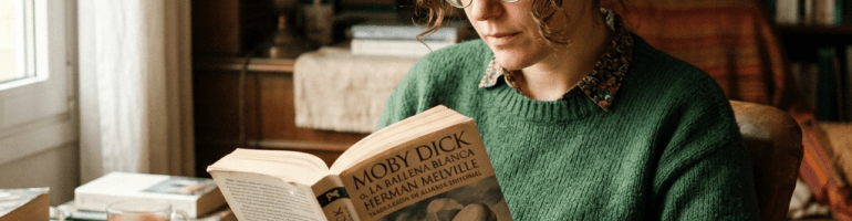 Woman in green sweater reading Moby Dick book indoors