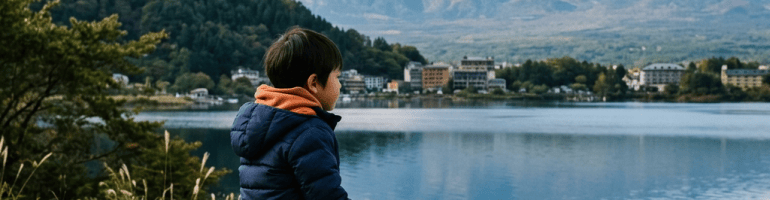 Child sitting on a bench beside a lake with snow-covered Mount Fuji
