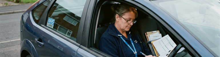 NHS carer writing paperwork inside a parked car
