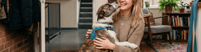 Woman kneeling and hugging an excited dog inside a cozy home