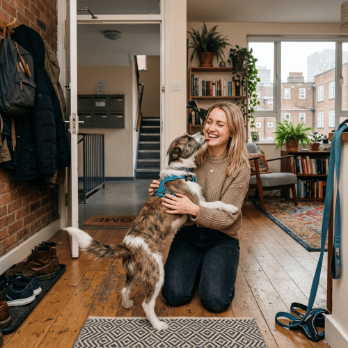 Woman kneeling and hugging an excited dog inside a cozy home