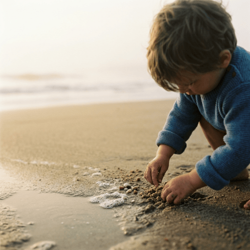 Young child in blue sweater playing with sand and shells on beach