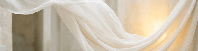 White fabric draped across a sunlit stone interior with arched openings