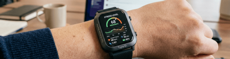 Smartwatch displaying “STRESS LEVEL 68 MODERATE” on a wrist at an office desk
